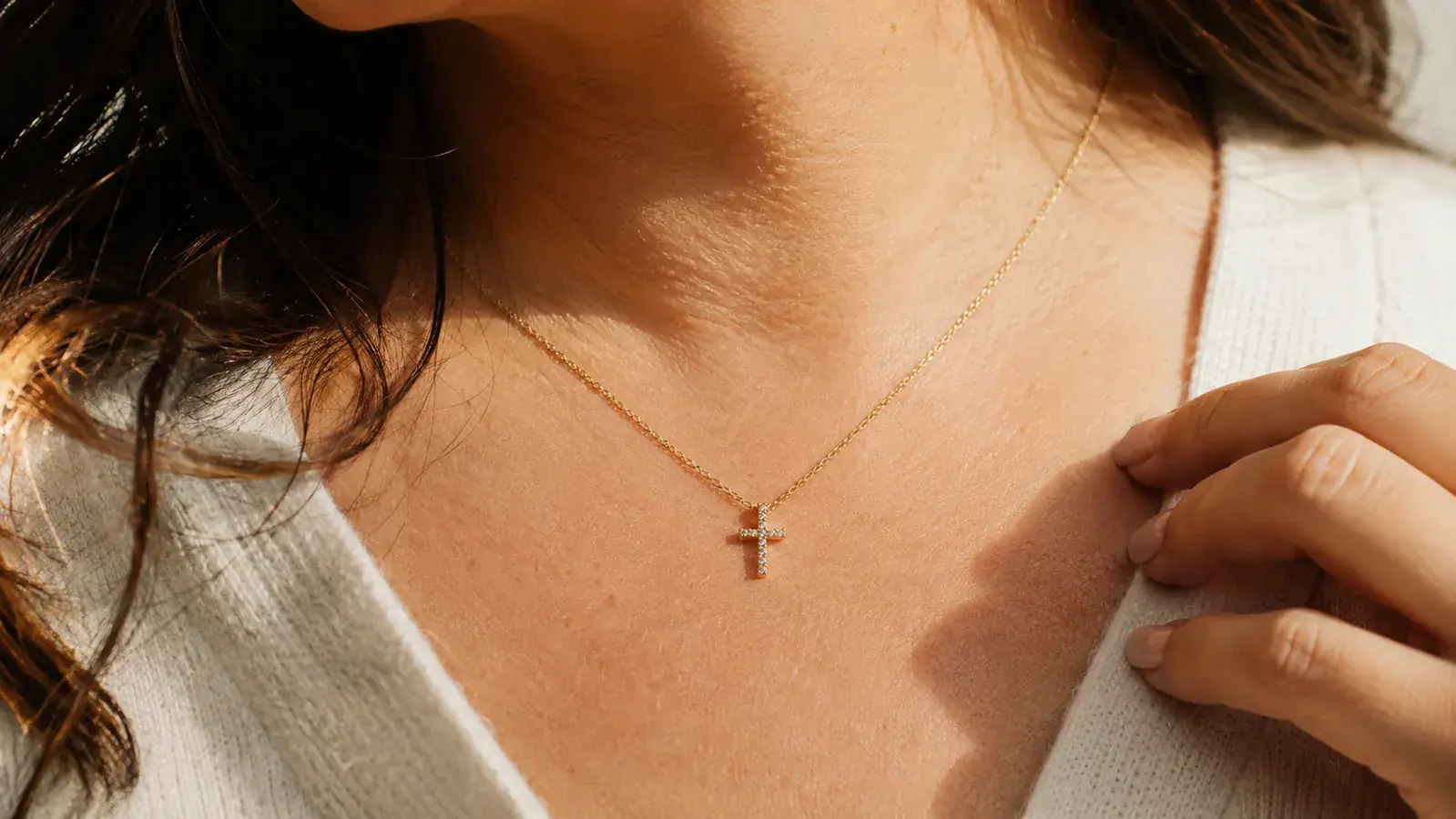 Close-up of a gold cubic zirconia cross pendant against a woman's collarbone, catching afternoon light